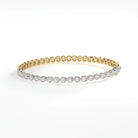 A slim bracelet that is half rose gold with round-cut diamonds, half on white gold with pear-cut diamonds, all bezel set, on a white background