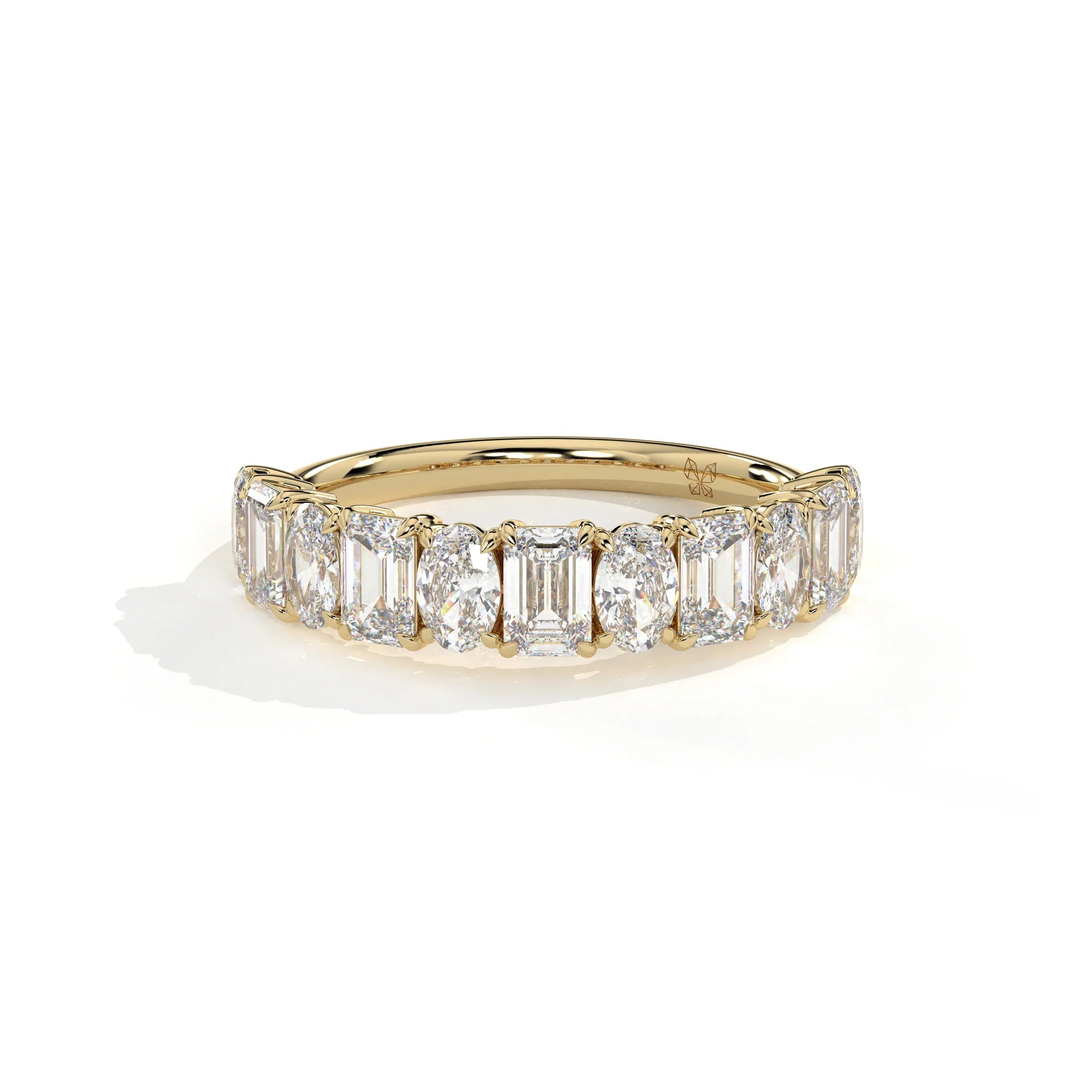 A yellow gold eternity ring featuring a row of baguette and oval-cut clear diamonds, photographed on a clean white background with a soft shadow.