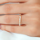A close-up of a hand wearing a slim yellow gold band ring with three small clear round-cut gemstones set in a row.
