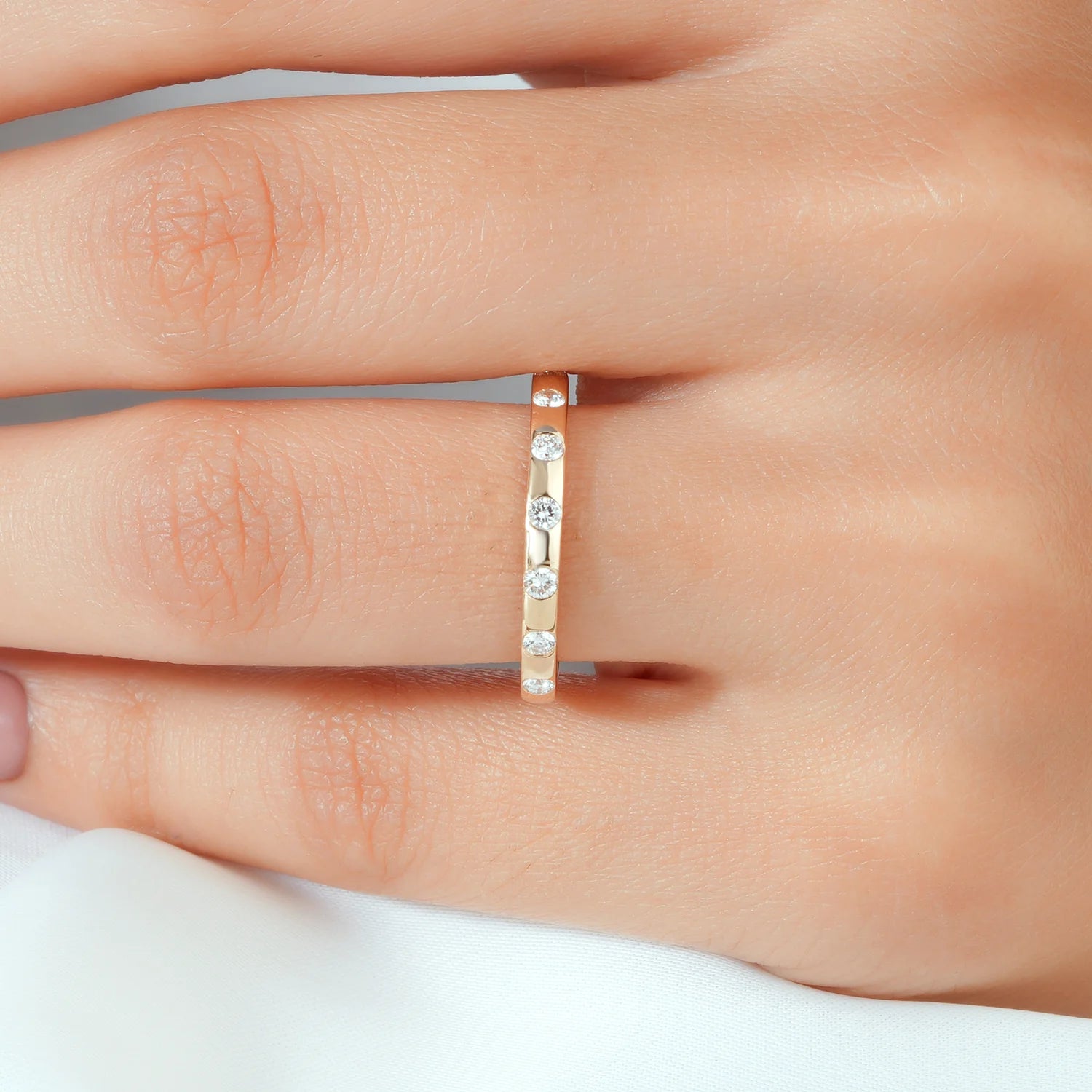 A close-up of a hand wearing a slim yellow gold band ring with three small clear round-cut gemstones set in a row.