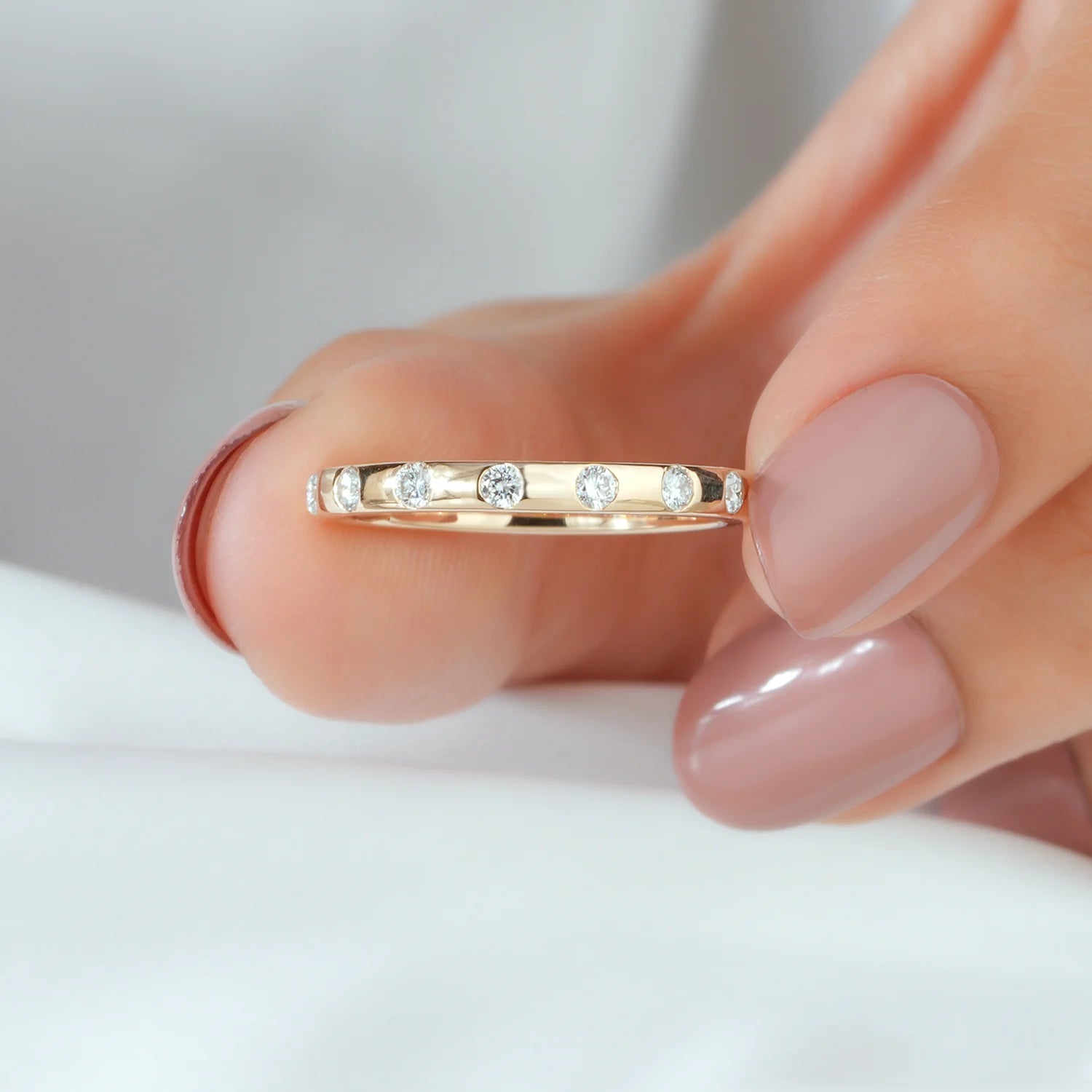 Gold ring with small diamonds held by a finger against a neutral background