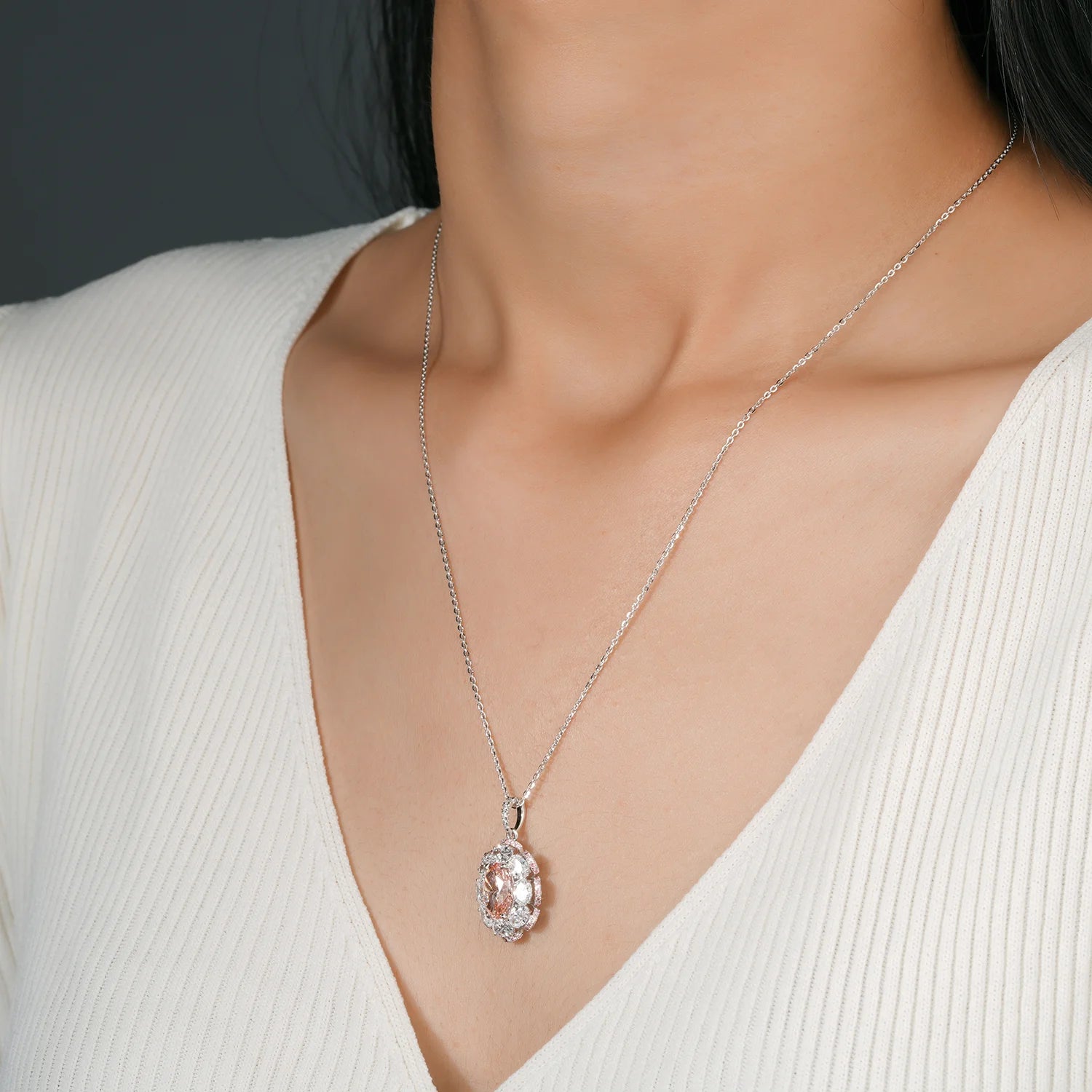 A close-up of a model wearing a delicate 10K white gold chain necklace with a teardrop-shaped pink diamond pendant set in a halo of brilliant cut diamonds.