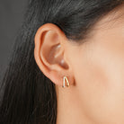 A close-up of a person's ear wearing a small curved huggie earring with a gold-toned band and a row of clear stones on one side.