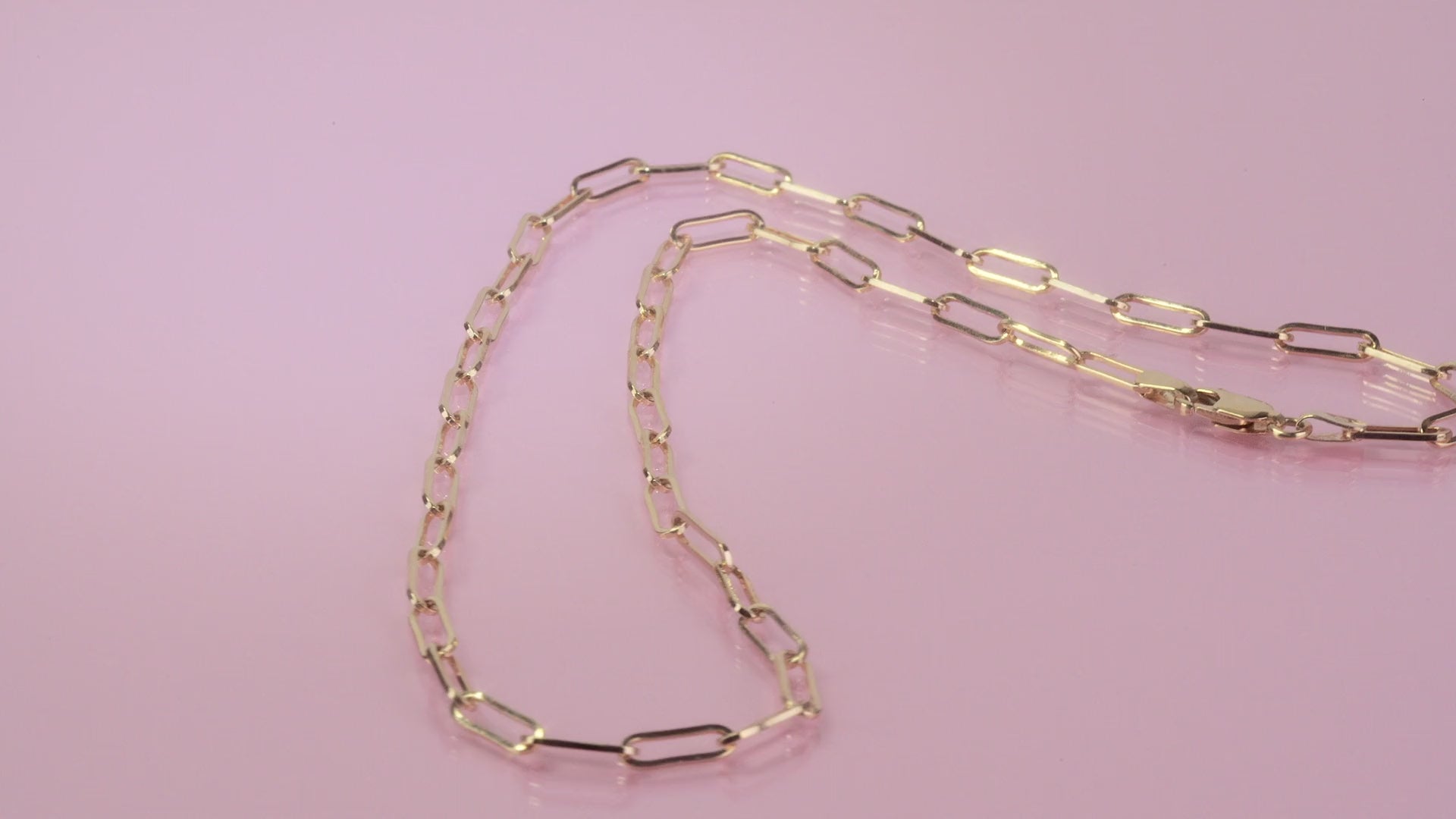 Gold chain necklace shines on a pink background.